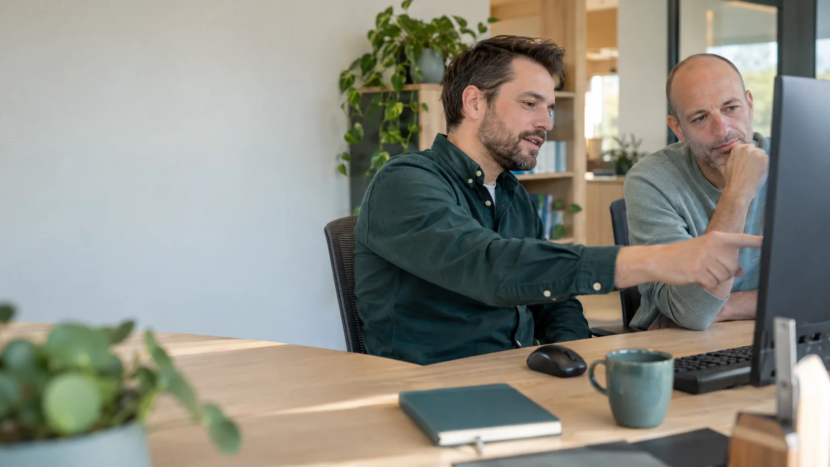 Twee mannen bekijken samen een computer terwijl één van hen uitleg geeft.
