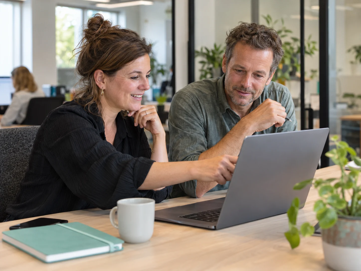 Twee collega’s werken samen aan een laptop op kantoor.